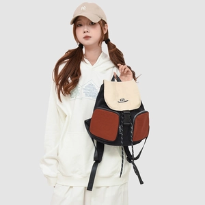 Detail view of the black and beige canvas backpack featuring orange-brown zip pockets and drawstrings
