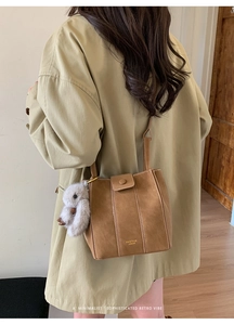 Detail of a brown suede bucket bag with white stitching and a plush bunny charm accessory