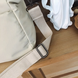 Detail of cream nylon crossbody bag featuring wide canvas strap and charcoal metal hardware