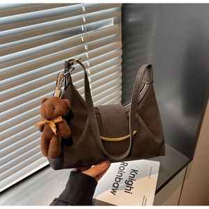 Detail view of a dark brown dumpling bag with a gold buckle and cute brown bear charm