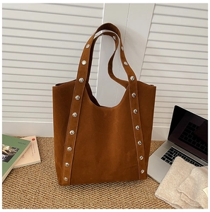 Detail of dark brown suede tote bag featuring silver rivet studs in a cozy office setting