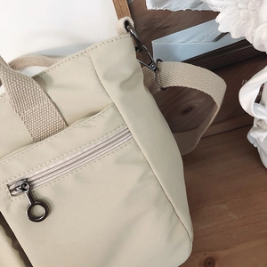Close-up of beige nylon tote bag showing durable twill texture and gunmetal zippers