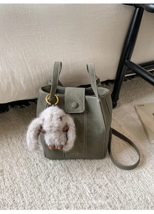Detail of dark green bucket bag with lychee leather texture and plush rabbit charm