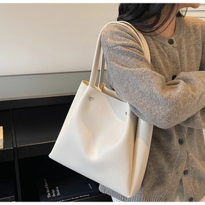 Detail view of a cream white minimalist tote bag with metal rivet accents and dual straps