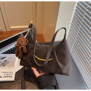 Detail of dark brown dumpling bag with golden crescent buckle and plush bear charm