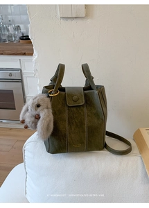 Close-up of green vintage bucket bag with plush rabbit charm and gold logo detail