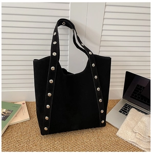 Detail of black suede tote bag with silver metal rivets on woven rug by a window