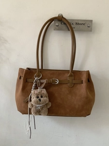 Brown vintage large tote bag with teddy bear charm hanging on a wall display
