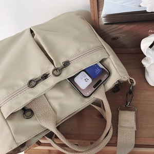 Detailed macro shot of beige nylon tote bag with metallic zippers and woven handles