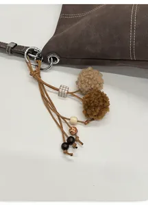Detalle de bolso tote de cuero marrón con elegantes pompones de peluche y colgantes