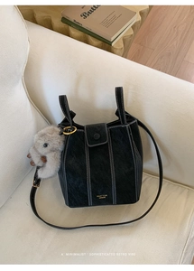 Detail of black bucket bag with white contrast stitching and grey rabbit plush charm