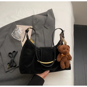 Detail view of black leather dumpling bag with gold crescent buckle and bear charm