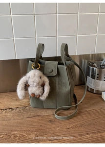 Detail of olive green leather bucket bag with gold logo and cute plush rabbit charm