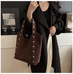 Detail view of deep brown tote bag with silver studs worn by a model in a black trench coat