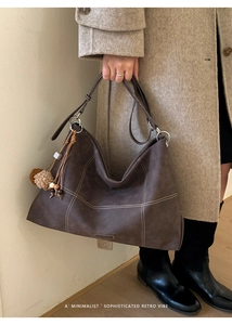 Detail of dark brown leather tote bag with white contrast stitching and tassel charm
