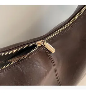 Gros plan sur la fermeture éclair dorée et le cuir marron texturé du sac à bandoulière