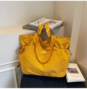 Detail of yellow nylon tote bag featuring YHAAYC logo and knotted rope handle