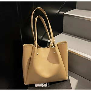 Detail view of large beige tote bag featuring silver rivet accents and smooth faux leather