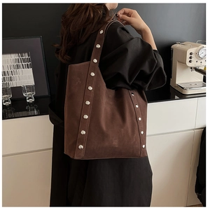 Brown suede tote bag with silver studs worn by a model in a modern cafe setting