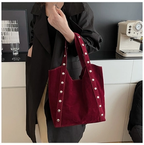 Deep burgundy suede tote bag with silver studs worn by a model in a black trench coat