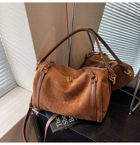 Détail d'un sac Boston en daim marron avec ferrures dorées sur une surface sombre