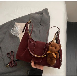 Detail of burgundy half-moon bag with gold metal handle and plush bear charm