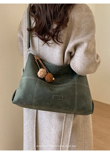 Close-up of olive green tote with white contrast stitching and plush ball charm