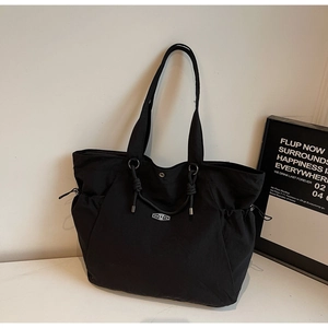 Detail of black large-capacity tote bag featuring side drawstrings and logo plaque