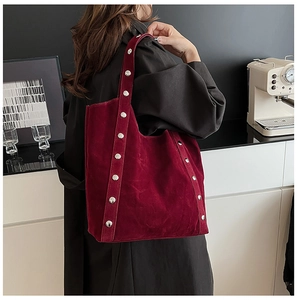 Detail of burgundy suede tote bag featuring silver rivet trim on the shoulder straps
