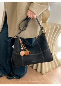 Detail of black suede tote bag with contrast white stitching and plush ball charm accessory