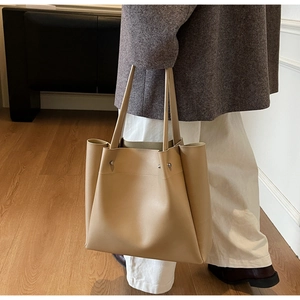 Minimalist beige leather tote bag detail with side fold design and silver rivet accents