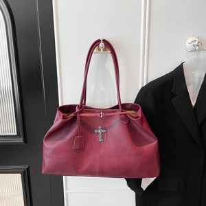 Dettaglio del pendente a croce argento e texture in pelle bordeaux su borsa shopper