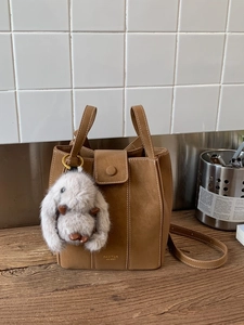 Retro tan leather bucket bag with white contrast stitching and cute plush bunny charm