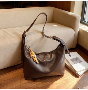 Gros plan d'un sac hobo marron foncé sur parquet avec un pendentif en perles