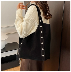Model wearing a large black matte tote bag with silver studs in a minimalist home setting