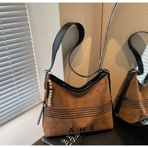 Detail view of brown velvet tote bag with embroidered AHE letters and beaded charm