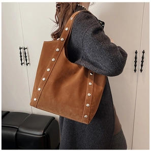 Brown suede tote bag with silver studs on straps worn by a model in a minimalist room