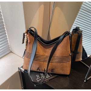 Detail view of brown suede tote bag featuring black embroidery and a wooden bead charm