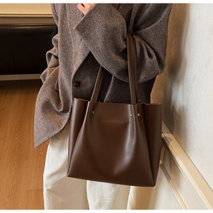 Detail of dark brown leather tote bag showing matte texture and side metal rivet accents