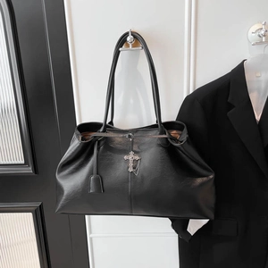 Dettaglio del pendente a croce gotica e catena metallica sulla borsa tote in pelle nera