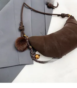 Détail d'un sac croissant marron vintage avec bandoulière tressée et pompon en fourrure