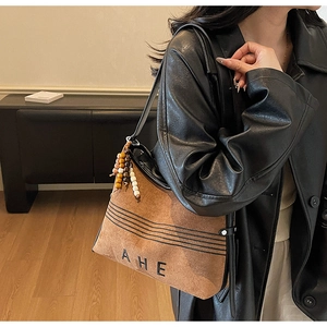 Detail view of brown suede tote bag featuring black AHE embroidery and beaded charm