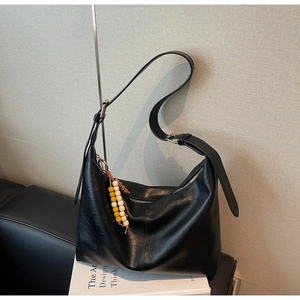 Vue détaillée du grand sac hobo noir avec un charme en perles colorées sur des livres blancs