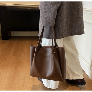 Detail of dark brown matte leather tote bag with side rivet accents shown on a model