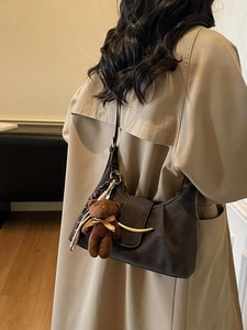 Deep brown crescent dumpling bag with gold buckle and plush bear charm on a model