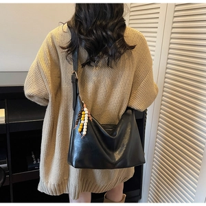 Détail du sac hobo en cuir noir brillant avec pendentif en perles et boucle métallique