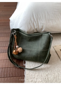 Detail of dark green matte tote bag with contrast stitching and fuzzy ball charm