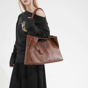Dettaglio della grande borsa tote in pelle marrone con ciondolo a croce sulla spalla