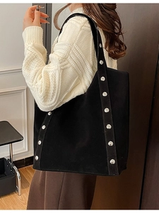 Large black suede tote bag with silver studs worn by a model in a warm interior setting