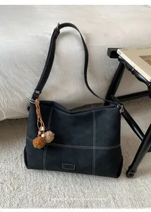 Detail of black tote bag with white contrast stitching and plush ball charms on a rug